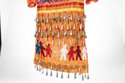 Le dos de la robe orange à clochettes montre huit figures humaines de différentes couleurs qui se tiennent par la main et forment une ligne qui encercle la robe. Des clochettes sont cousues sur la robe au-dessus et au-dessous des personnages.