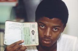 Un jeune homme noir fait face à la caméra, brandissant un livret ressemblant à un passeport.