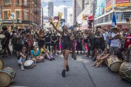 Une foule diversifiée se tient dans une rue du centre-ville, entourant une femme noire qui s’exprime dans un mégaphone.
