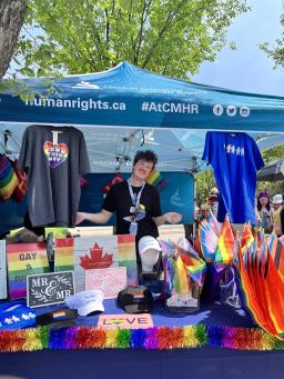 Three drag artists holding Pride-themed books are sitting in front of a rainbow-themed arch.