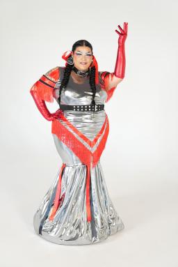 Une drag queen est vêtue d’une robe rouge et argentée et de gants rouges assortis.