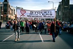 Deux femmes tiennent une grande bannière sur laquelle on peut lire « Stolen Sisters Memorial March » (Marche commémorative des sœurs volées) et dirigent un grand groupe de protestataires dans une rue de la ville.