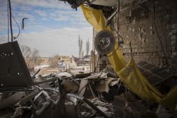 Des gravats et des débris sont éparpillés dans une salle d’opération détruite dans un hôpital. Une bâche jaune pend du plafond à côté d’une lampe suspendue. Le mur extérieur de la salle d’opération a disparu, exposant la salle d’opération à l’extérieur.