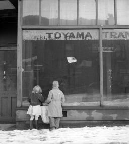 Photographie en noir et blanc de deux enfants regardant la vitrine d’un magasin abandonné.