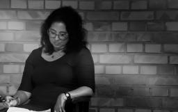  Portrait en noir et blanc d’une femme aux cheveux bouclés foncés qui regarde un document posé sur ses genoux.