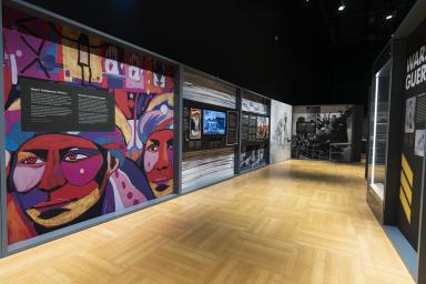 Une galerie muséale dont le panneau le plus visible est une œuvre d’art colorée représentant des visages et des symboles autochtones.