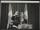 Une photographie en noir et blanc de Nelson Mandela debout derrière un podium. Il sourit et fait signe de la main.