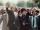 Nelson Mandela, an older black man with graying hair, forms a raised fist with his right hand and holds it above his head. With his left, he is holding hands with Winnie Mandela, a black woman with dark hair. She is smiling and has formed a raised fist with her left hand, mirroring Nelson Mandela’s raised fist. A large crowd is gathered behind them.