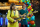 Deux guitaristes en tenues vives et colorées chantent dans des microphones devant une arche de ballons.