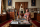 Une femme est à genoux près d’une table basse entourée de livres et d’objets de famille.