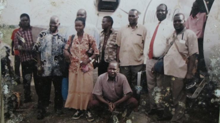 Un groupe de neuf personnes se tient devant un fond blanc dans un décor extérieur et pose pour la photo.