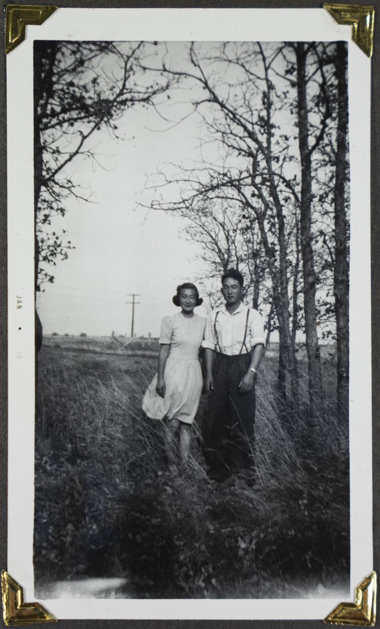 Un jeune couple canadien d’origine japonaise pose dans un champ avec des arbres en arrière-plan. Visibilité masquée.
