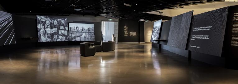  Une galerie de musée où on voit des photographies projetées sur de grands écrans. Il y a des fauteuils au milieu de la pièce. Visibilité masquée.