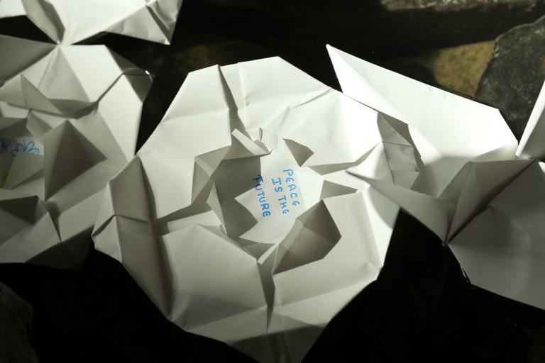  Folded paper lilies floating in water. “Peace is the future” is written in the centre of one lily. Visibilité masquée.