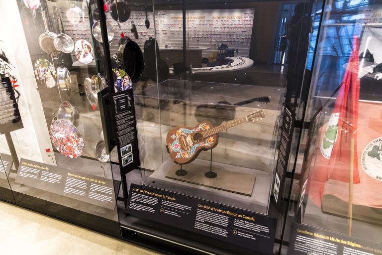 Une guitare est exposée dans une vitrine au-dessus d’un panneau sur lequel on peut lire « La vérité et la réconciliation au Canada ». Visibilité masquée.
