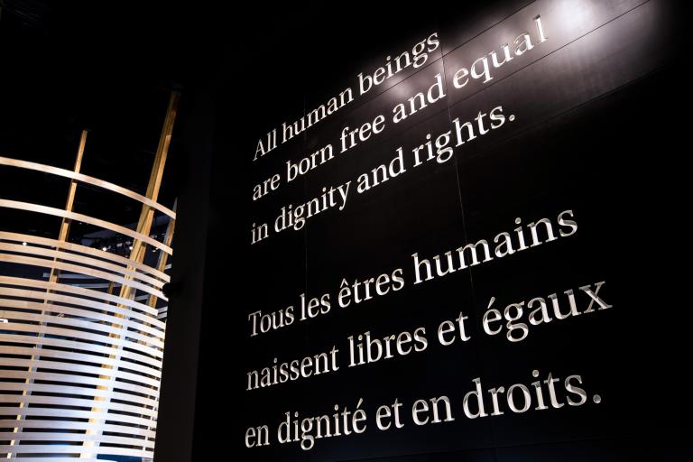 Du texte blanc en grand format sur un mur noir : « Tous les êtres humains naissent libres et égaux en dignité et en droits. »