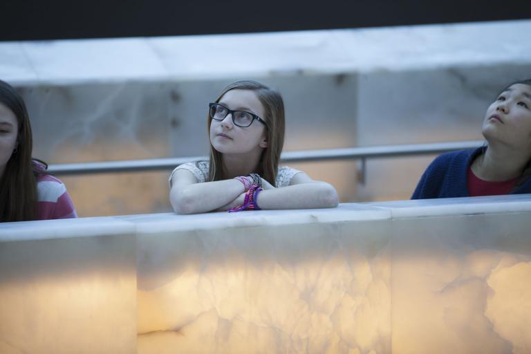  Three young people leaning on a glowing alabaster ramp and looking up. Visibilité masquée.