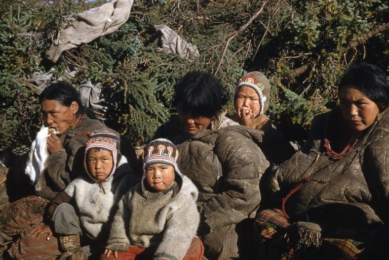 Un groupe de femmes et d’enfants assis. Les deux enfants en avant regarde vers l’objectif. Visibilité masquée.