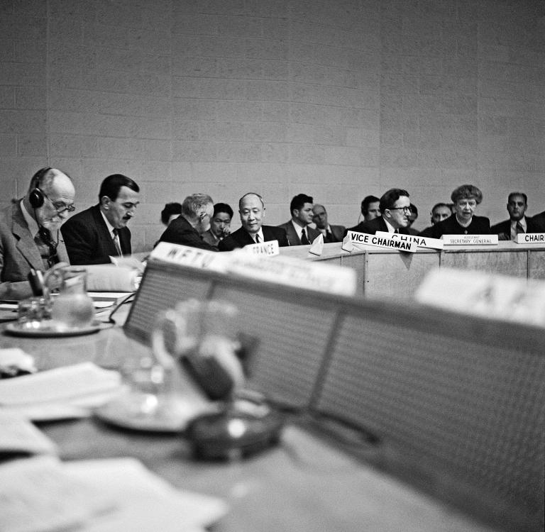 Photo d'archives en noir et blanc d'un groupe de personnes assises autour d'une table de conférence.