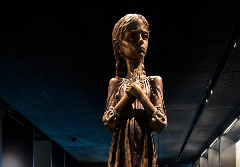 A statue of a young girl clutching stalks of wheat. Visibilité masquée.