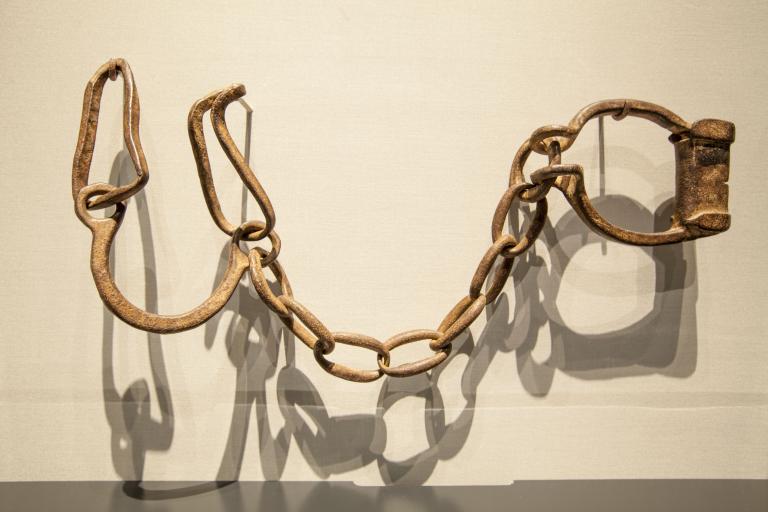 Des menottes rouillées sont suspendues sur un mur blanc. Visibilité masquée.