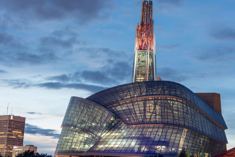 Un édifice de forme inhabituelle avec une tour de verre, illuminée de rouge, au-dessus d'un « nuage » constitué de centaines de panneaux de verre. Visibilité masquée.