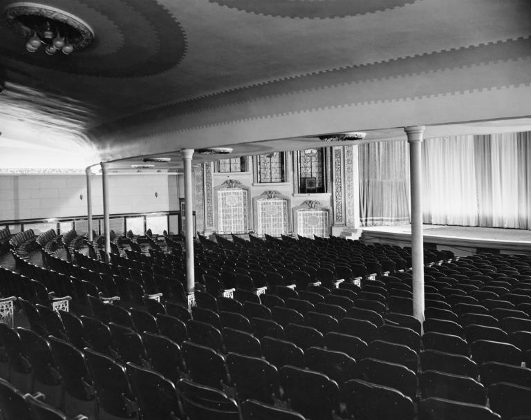 Une photo en noir et blanc de l’intérieur d’une salle de théâtre de style ancien, vide.