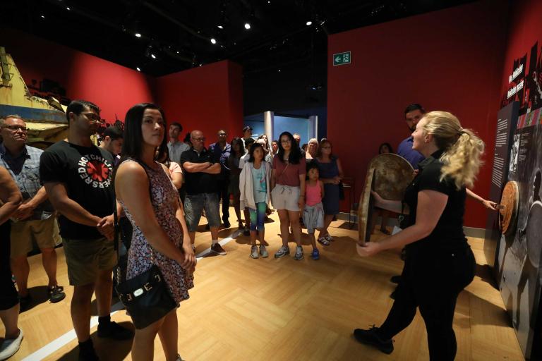 Des personnes debout qui écoutent une guide-interprète du Musée. Visibilité masquée.