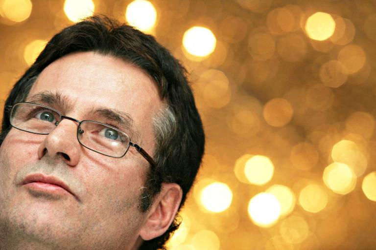 Gros plan du visage d’un homme regardant vers le haut d’un air réfléchi. Il porte des lunettes et il y a des taches de lumière floues à l’arrière-plan. Visibilité masquée.