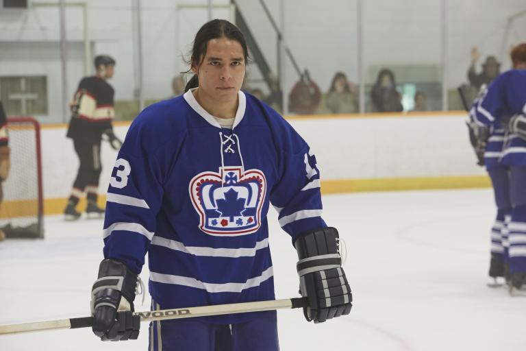 A young man in a blue hockey uniform with a crown logo on an indoor ice rink. Visibilité masquée.