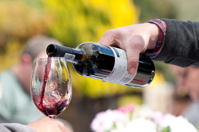 Du vin rouge est versé d'une bouteille dans un verre. Visibilité masquée.