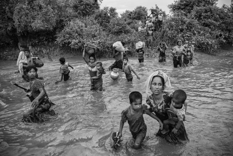 Un groupe de femmes et d’enfants rohingyas marchent dans un canal où l’eau est de deux à trois pieds de profondeur, en transportant leurs effets personnels.