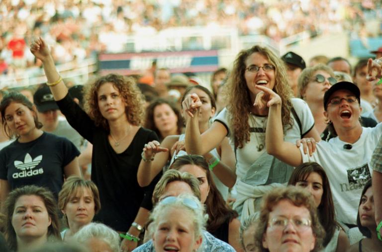 Une foule de femmes, regardant un spectacle hors champ. Un bon nombre d’entre elles sourient, et certaines ont les bras levés. On peut voir une foule plus nombreuse assise dans un stade derrière elles.