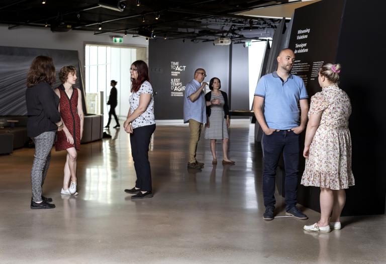 Des petits groupes de personnes en conversation debout dans un espace d’exposition de Musée. Visibilité masquée.