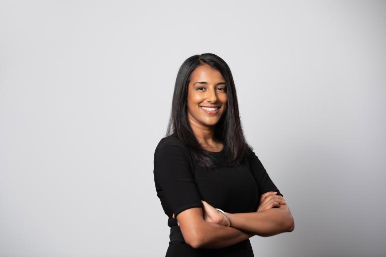 Le portrait d’une femme souriante aux bras croisés devant un arrière-plan blanc. Visibilité masquée.