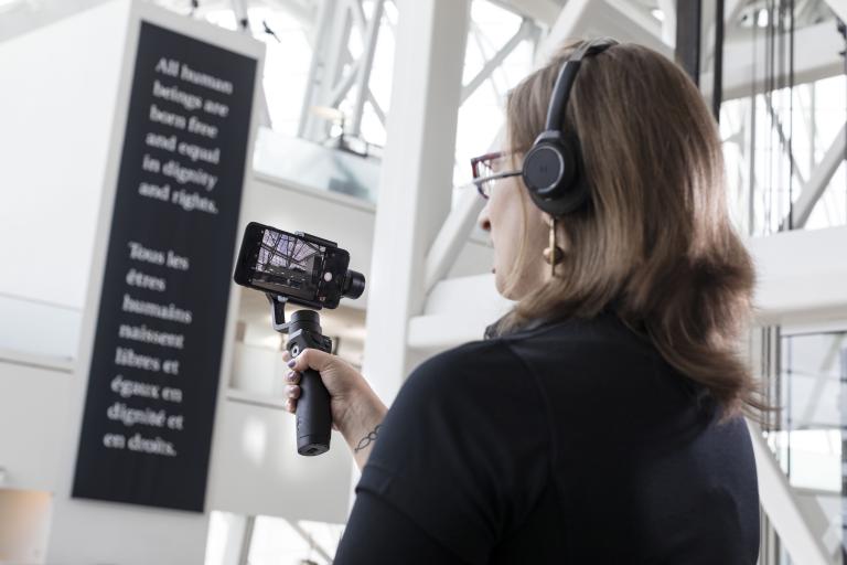 Une femme tient une barre avec un téléphone portable fixé au bout et utilise l'écran pour regarder quelque chose hors champ. Visibilité masquée.