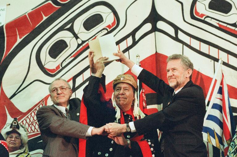 Trois hommes se serrent les mains tout en tenant un document au-dessus de leur tête.