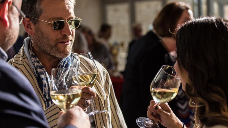 Des invités à une soirée discutent en tenant des verres de vin blanc. Visibilité masquée.