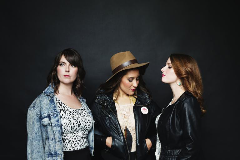 Trois femmes posent devant un mur noir. Visibilité masquée.