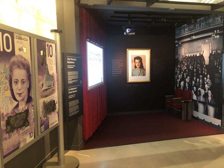 Une exposition muséale qui ressemble à un cinéma de vieux style. D’un côté, on voit de grandes images représentant un billet canadien de 10 $ sur lequel figure le visage d’une femme. Visibilité masquée.