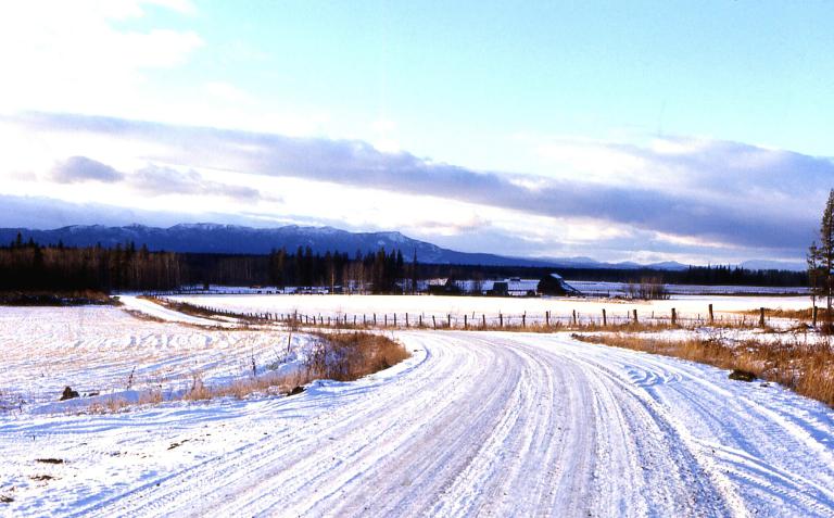 Une route de campagne couverte de neige; on voit des montages au loin. Visibilité masquée.