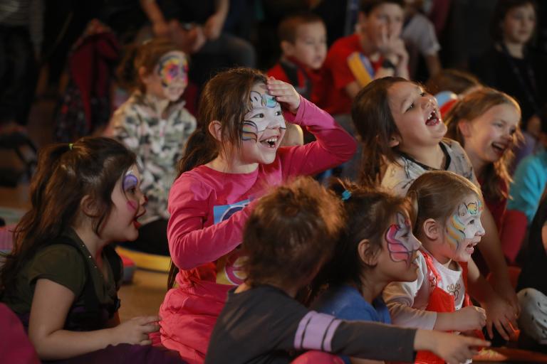Un groupe d’enfants aux visages peints rient et font des gestes. Visibilité masquée.
