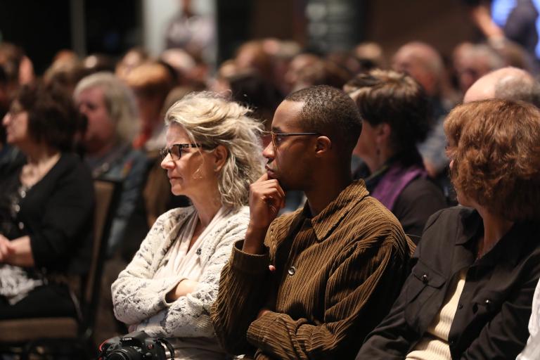 A crowd of people sitting and listening intently. Visibilité masquée.