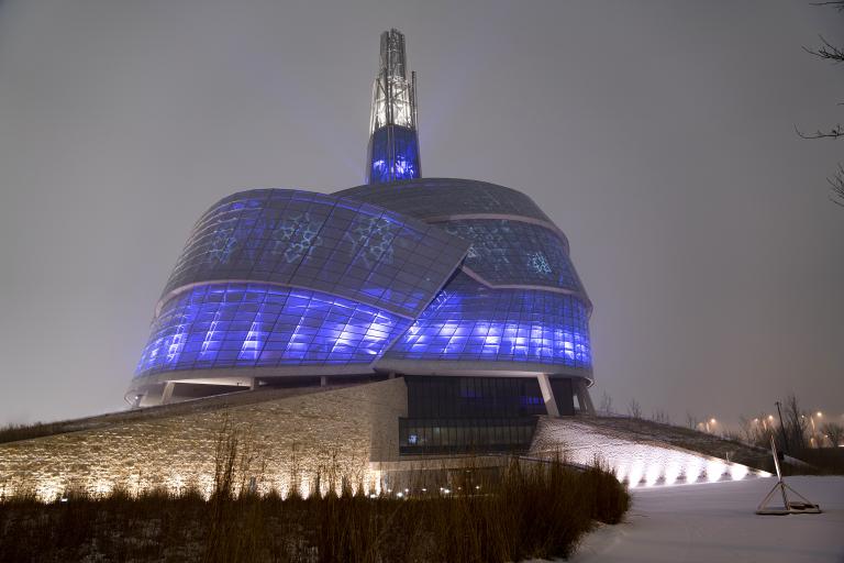  Un édifice recouvert de panneaux de verre illuminé de bleu et de violet. Des motifs de flocons de neige sont également projetés sur les fenêtres. Visibilité masquée.
