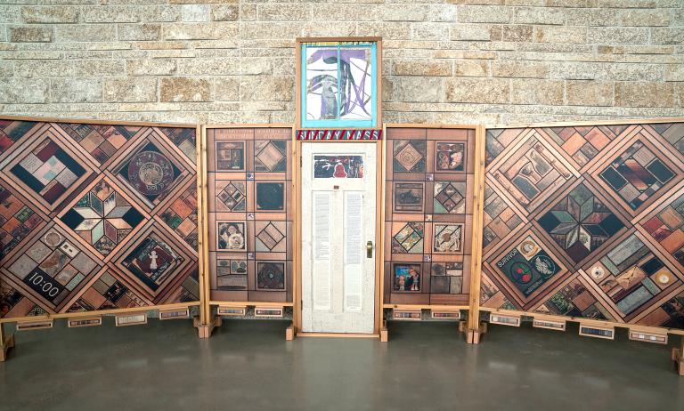 Une porte blanche décorée de texte et d’images, flanquée de panneaux de bois verticaux recouverts de motifs d’images.