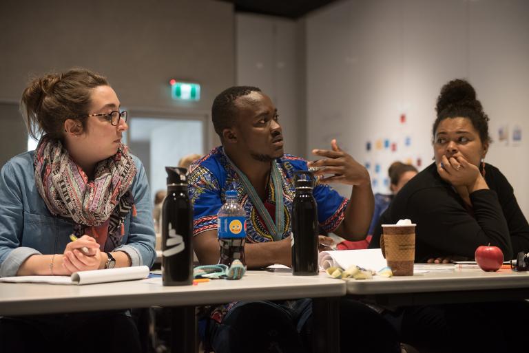 Trois personnes sont assises à une table couverte de bouteilles d'eau, de tasses à café et de blocs de papier. Visibilité masquée.