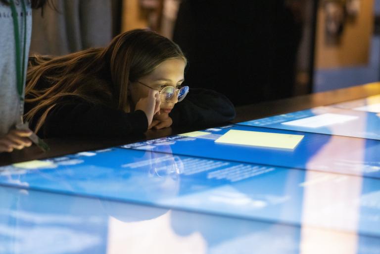 A girl looks at a horizontal interactive display with interest. Visibilité masquée.