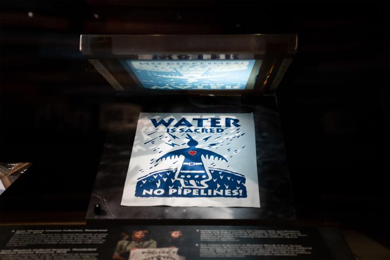 Sur un cadre de sérigraphie, on voit une impression terminée qui dit « L’eau est sacrée, non aux pipelines! ».