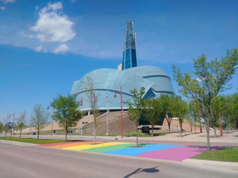 A rainbow crosswalk in front of the Canadian Museum for Human Rights on a sunny day Visibilité masquée.