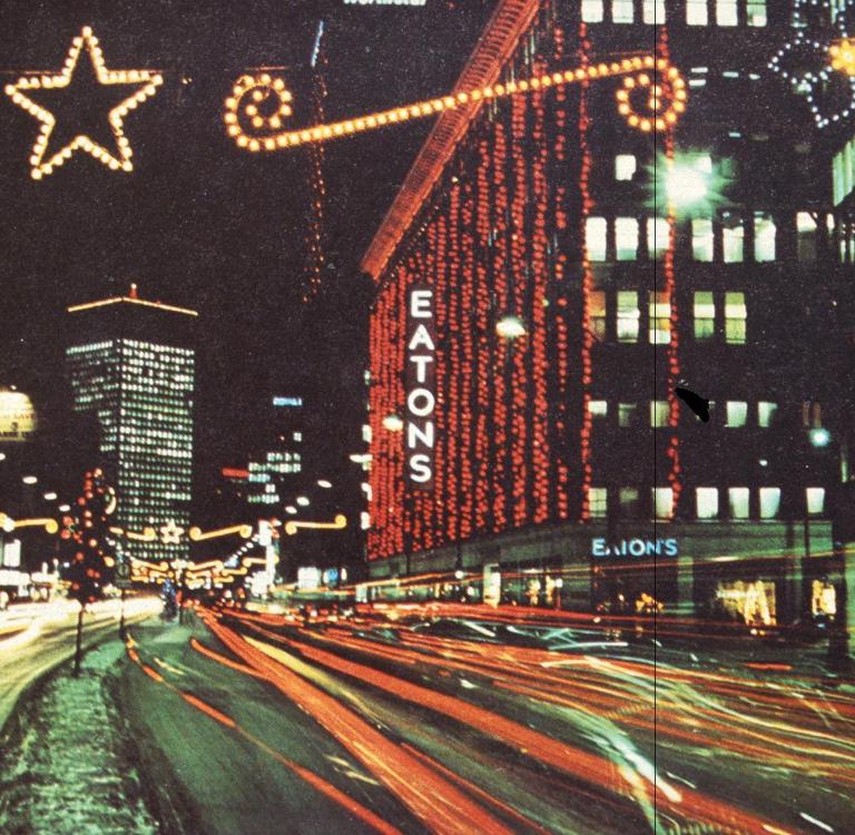 Photo du centre-ville de Winnipeg à la fin des années 1960 où l’on voit l’édifice Eatons décoré de nombreuses lumières de Noël. Visibilité masquée.